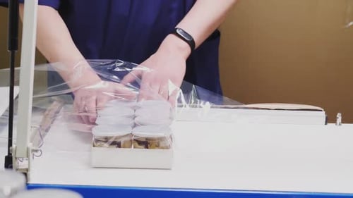 Employee Packs Box of Jars with Foil at Table in Workshop