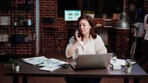 Woman Answering Phone Call While Working in Office at Computer Desk
