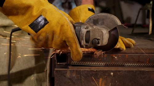 Men's Gloved Hands Cut a Piece of Iron Pipe with Sparks with a Grinding Machine