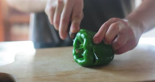 Chef cutting fresh, raw, green capsicum on chopping board, in the kitchen. Close up.