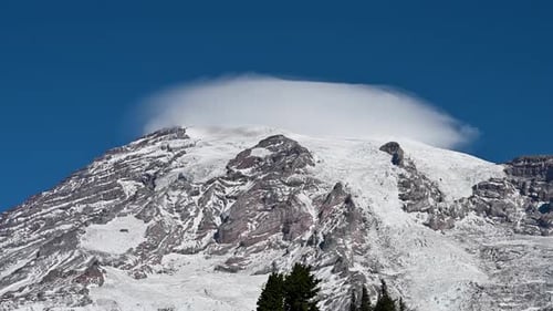 Aerial drone shot of snow-covered mountain peak with lenticular cloud formation above summit.