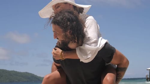4k video footage of a young man giving his girlfriend a piggyback ride at the beach