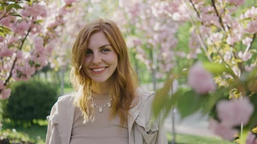 Portrait of a Beautiful Young Redhaired Woman A Girl Walks in the Park Among Pink Blossoming Sakura