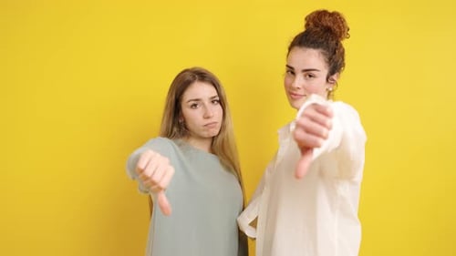 Women Give Thumbs Down Against Yellow Background