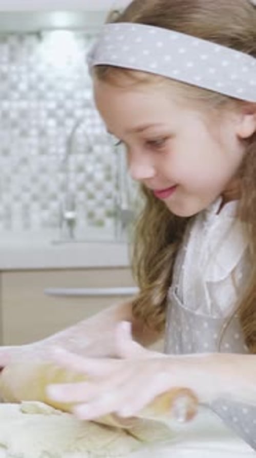 Young Girl with Curly Hair is Baking Cookies in a Bright Kitchen with Flour on the Countertop