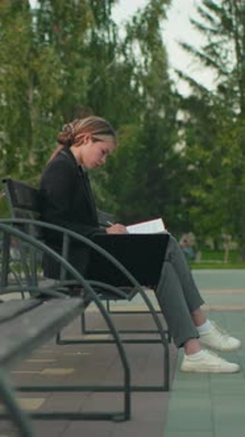 Student Reading Red Folder Outdoors with Laptop in Quiet Park Setting