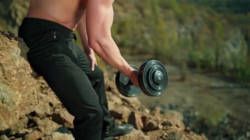 Sportsman pumping arm muscles on rocky background.