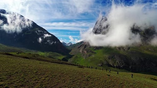 Eine Gruppe von Menschen läuft auf einem grasbewachsenen Hang mit einem bewölkten Himmel im Hintergrund