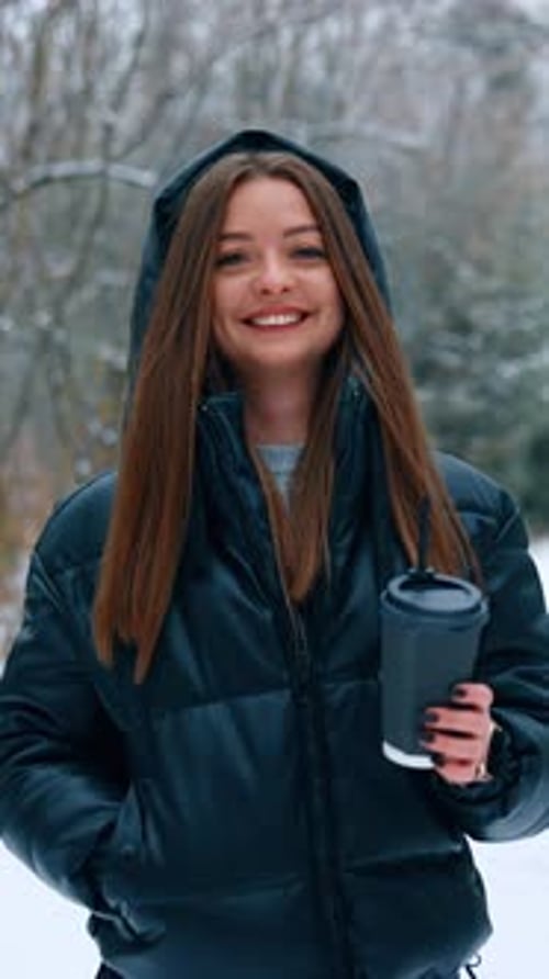 Happy relaxed woman with long brunette hair walks by the park in winter.
