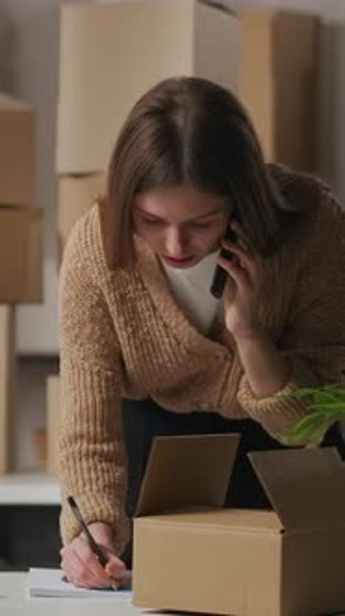 Woman on Phone Taking Notes Near Shipping Box