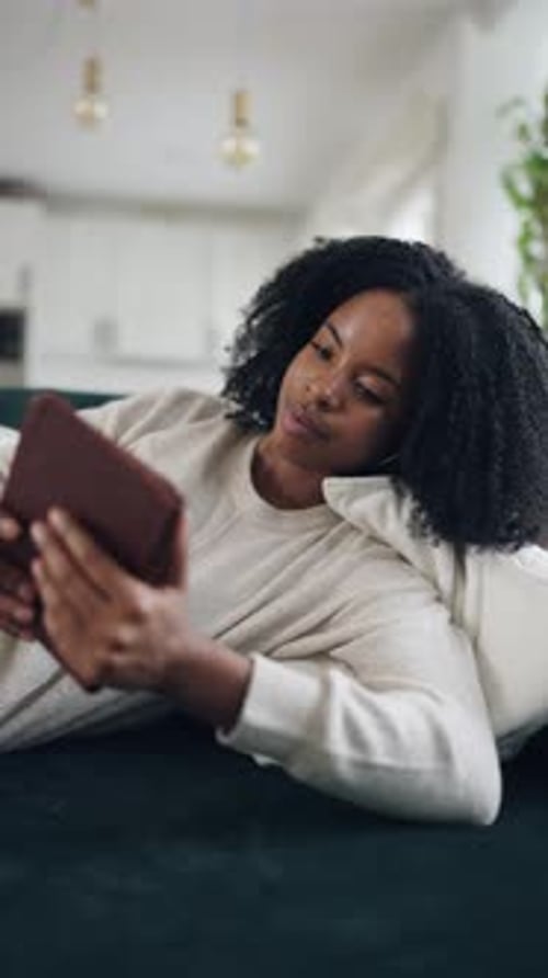 Relaxed African American Woman Reading an Ebook on the Sofa