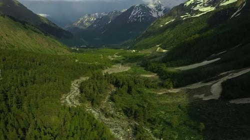Valley with a River Running Through It Surrounded By Mountains and Trees with Snow on the Tops