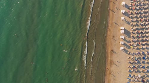 A crowded beach with umbrellas and people swimming in clear green water, aerial view