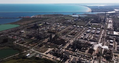 Aerial view of a large industrial oil refinery complex located near the coastline. Multiple storage