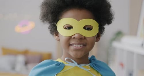 Closeup Portrait of Sweet African American Child in Superhero Mask and Cape Standing at Home Smiling