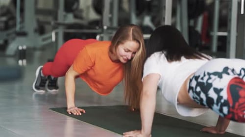 Sportliche Frau quetscht sich unter Aufsicht eines Trainers im Fitnessstudio