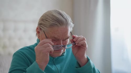 Senior Woman Puts on Glasses Indoors