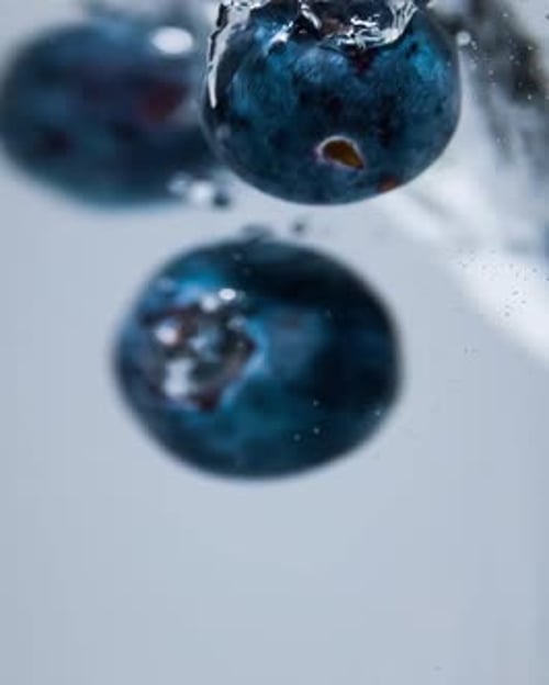 Super Slow Motion Shot of Fresh Blueberries with Splashing Water Isolated on White Blue Background