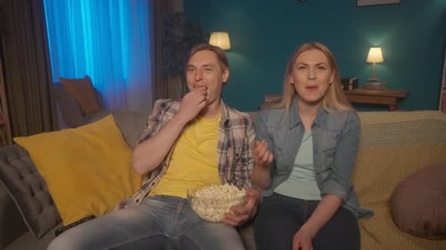 A Married Couple Sits on the Couch with a Plate of Popcorn and Watching a Movie Man and Woman