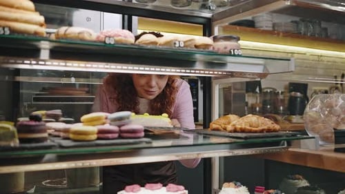 Smiling Woman Examines Desserts in Bakery Display Case