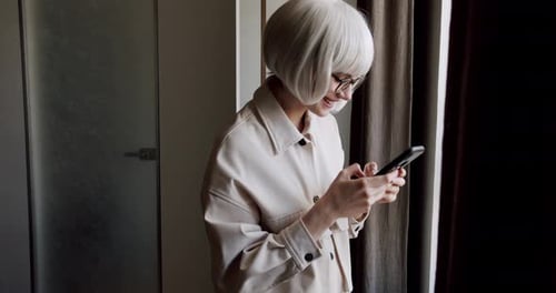 Smiling Woman Uses Phone Inside Near Window