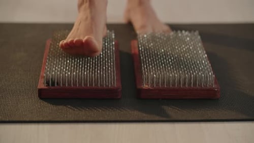 Vista recortada de uma mulher descalça pisando na prancha de sadhu, pés femininos nas unhas afiadas, prática de ioga