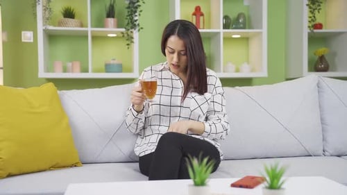 Woman Drinks Tea, Takes Pill on Sofa