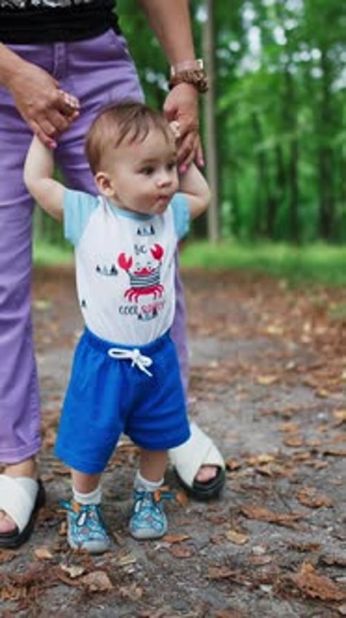 Little toddler stepping slowly looking around. Mommy's holding her baby helping him to walk.