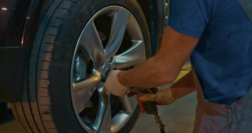 Automechaniker verschraubt das Autorad eines angehobenen Automobils mit einem pneumatischen Schraubenschlüssel