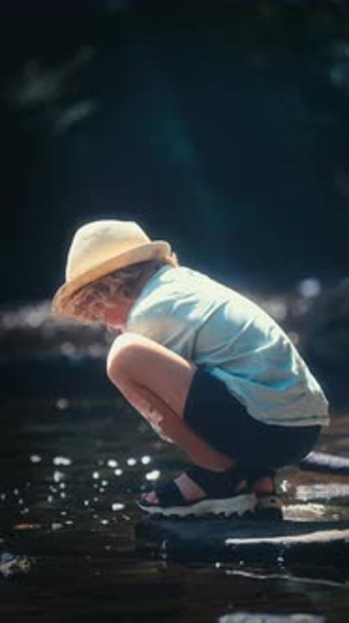 Young Boy Looking At The Creek Water While Squatting On A Rock