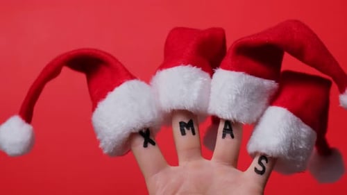 Fingers Dressed in SantaClaus Redwhite Hats and Word Text XMAS on Red Background