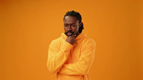 Young African Man with Hand on Chin Thinking About Question on Yellow Background