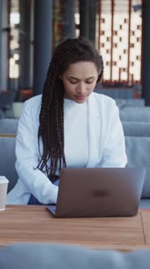 Jolie jeune femme indépendante heureuse assise sur un banc travaillant avec un ordinateur portable dans une ville urbaine moderne