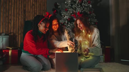 Friends Opening Christmas Gift by Glowing Tree