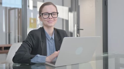 Woman Smiling While Working on Laptop in Office