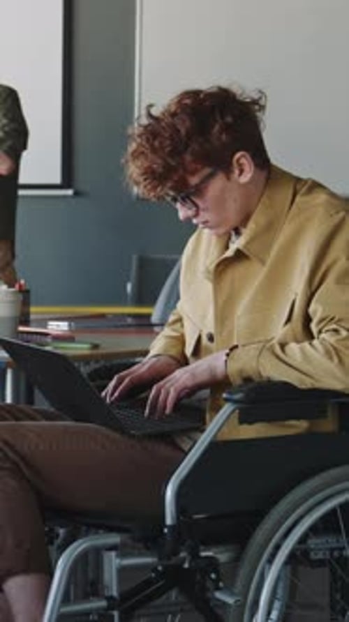 Concentrated Man in Wheelchair Typing on Laptop at Work in Office