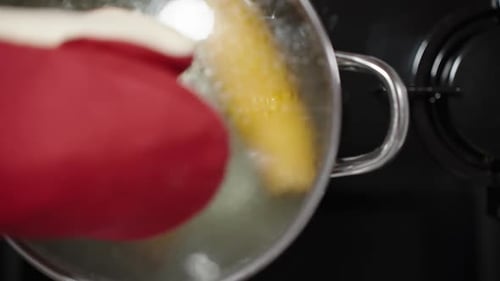 The corn is boiling in the simmering water, and from a top-down view, the lid is slowly lifted off i