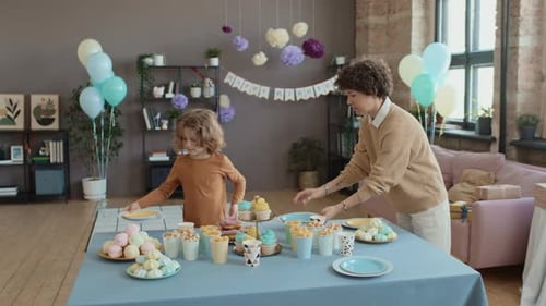 Caucasian Mom and Son Laying out Sweets on Table for Kids Birthday Party