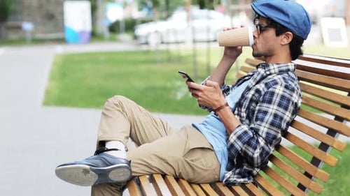 Man texting on smartphone with coffee in city street bench scene
