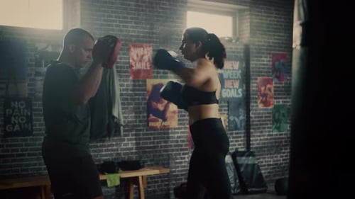 Fit Athletic Woman Kickboxer Punches and Hits the Punching Pads During a Workout in a Loft Gym. She