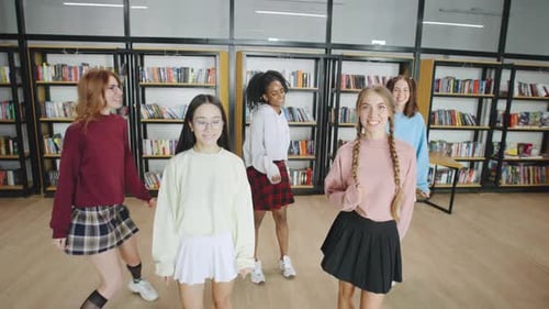 Grupo de universitárias multirraciais, blogueiras, líderes de torcida, amigas dançando alegremente na biblioteca durante