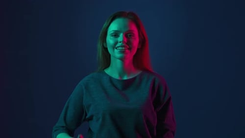 Portrait of a Young Redhaired Woman in a Studio on a Blue Background in Pink and Green Neon Light
