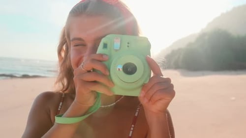 Young Caucasian Woman Tourist with Green Camera Takes Photo From Sunny Sea Beach