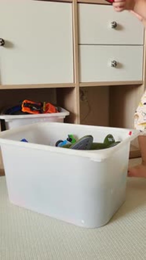 The child puts the toys in the box after playing, cleaning the room. Baby aged two years (two year o