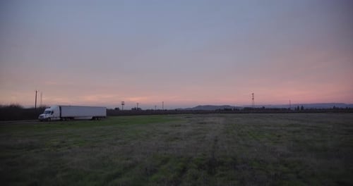 A pastel sky over the Sierra Nevada mountains with power lines and a 18 wheel truck in the foregroun