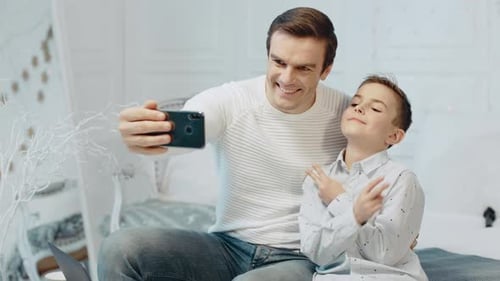 Cheerful father and son taking selfies in bedroom