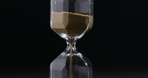 Deadline. Hourglass with flowing sand on black background, closeup