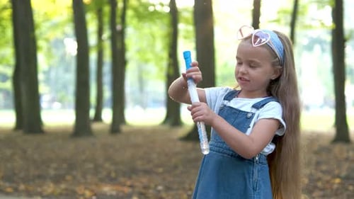 Little Happy Child Girl Blowing Soap Bubbles Outside in Green Park