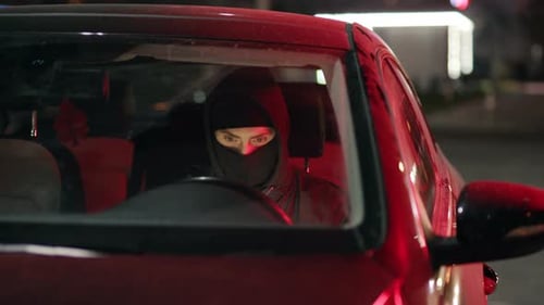 Un personnage mystérieux dans une voiture rouge vu tard dans la nuit, évoquant un sentiment d'intrigue et de suspense