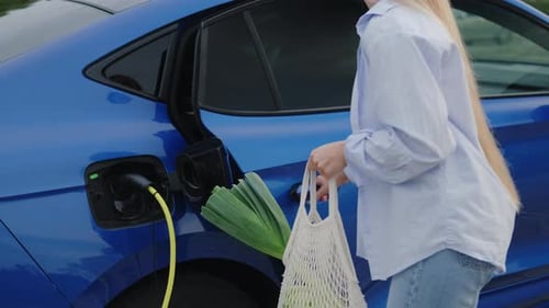Una señora coloca una bolsa reutilizable con la comida en un coche eléctrico